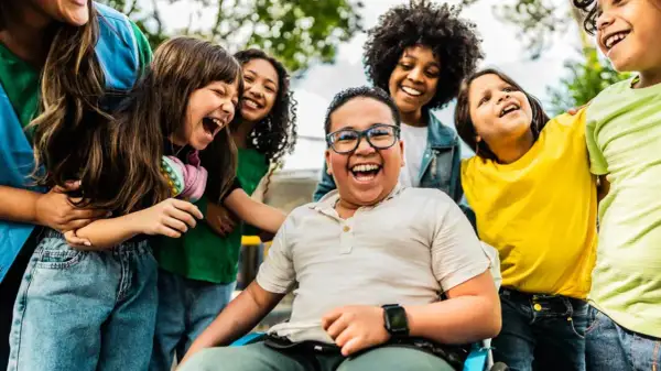 Fröhliche Kinder lachen und umarmen sich. Ein Junge im Rollstuhl strahlt. Wann ist Weltkindertag? An diesem Tag feiern wir alle Kinder!