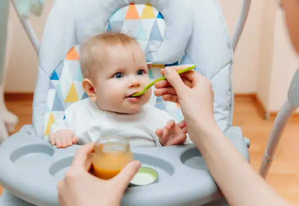 Ein süßes Baby von 6 Monaten sitzt im Hochstuhl und bekommt Brei gefüttert.