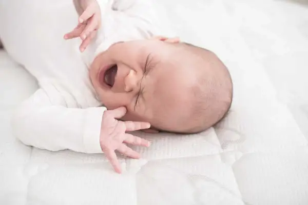 Ein Baby mit weit geöffnetem Mund und geschlossenen Augen, das sich im unruhigen Schlaf windet. Seine kleinen Hände sind nach oben gestreckt.