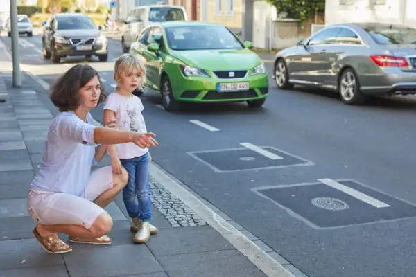Frau erklärt Kind Verkehrsregeln am Zebrastreifen. Verkehrserziehung im Kindergarten ist wichtig.