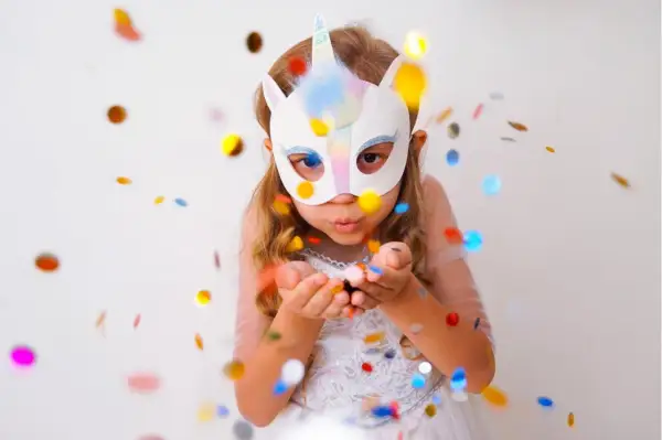 Kind mit Einhorn-Maske pustet Konfetti. Perfekt für Ideen zum Masken basteln, Vorlagen ausdrucken und eine magische Feier.