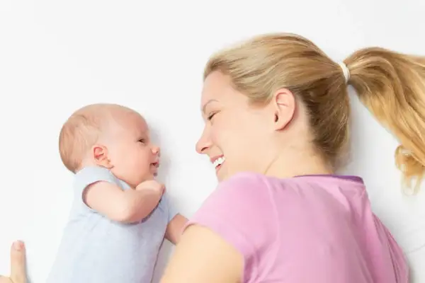 Ein lächelnder baby 2 wochen alt schaut seine Mutter an. Sie liegt neben ihm und lächelt zurück.