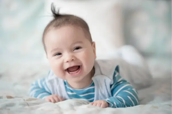 Ein fröhliches Baby, 21 Wochen alt, liegt auf dem Bauch und lacht herzhaft.