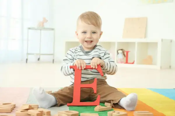 Ein lächelnder Junge hält den roten Buchstaben "E". Vielleicht ein zukünftiger Elias oder Emil, einer der vielen Jungennamen mit E.