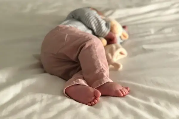 Ein Baby schläft auf einer weißen Decke, die Füße nach vorne gestreckt. Es ist ein Zeichen für einen Wachstumsschub, wenn Babys so tief und fest schlafen.