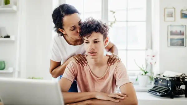 Mutter küsst Sohn auf die Stirn, legt Hände auf seine Schultern. Sie liebt ein narzisst seine Kinder, doch hier wirkt es wie echte Zuneigung.