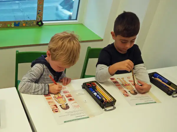 Zwei Jungen lernen in der vorschule kita etwas über den menschlichen Körper. Sie malen und beschriften Arbeitsblätter.