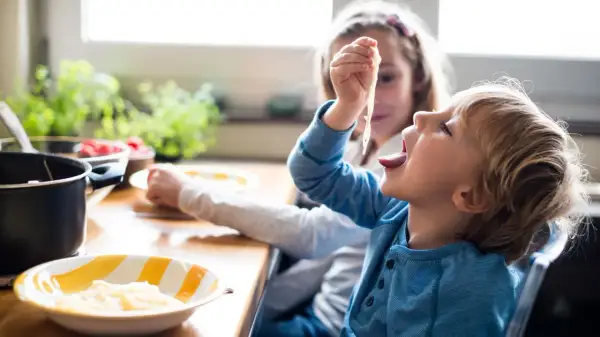 Große Schwester versucht, den kleinen Bruder zum Essen zu überreden, der nicht essen will.