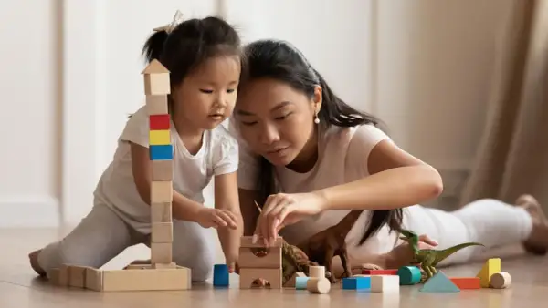 Mutter und Kind bauen mit Holzklötzen und Dinosauriern. Feinmotorik Kinder wird spielerisch gefördert.